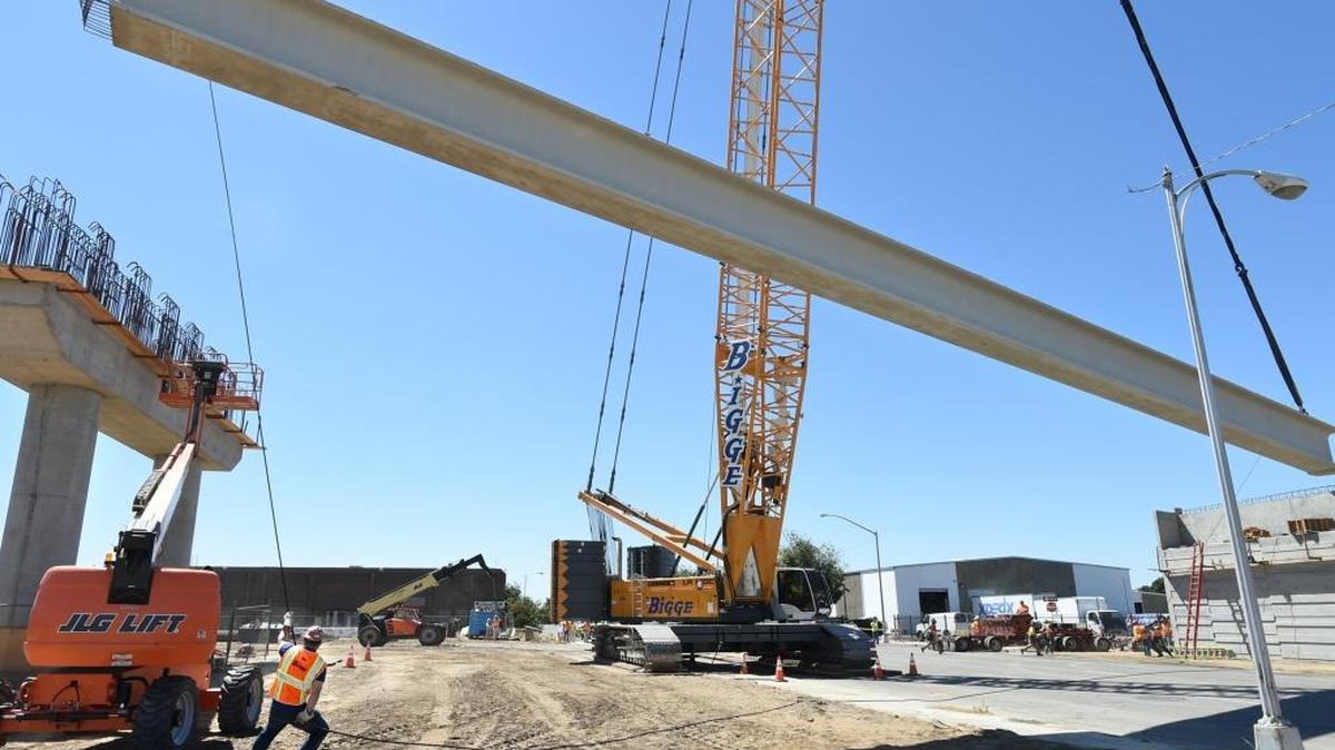A worker uses brawn and finesse to tug a concrete-and-steel girder into place as a giant crane gently lowers it, during construction of the new Tuolumne Street bridge in downtown Fresno in this June 2016 file photo.