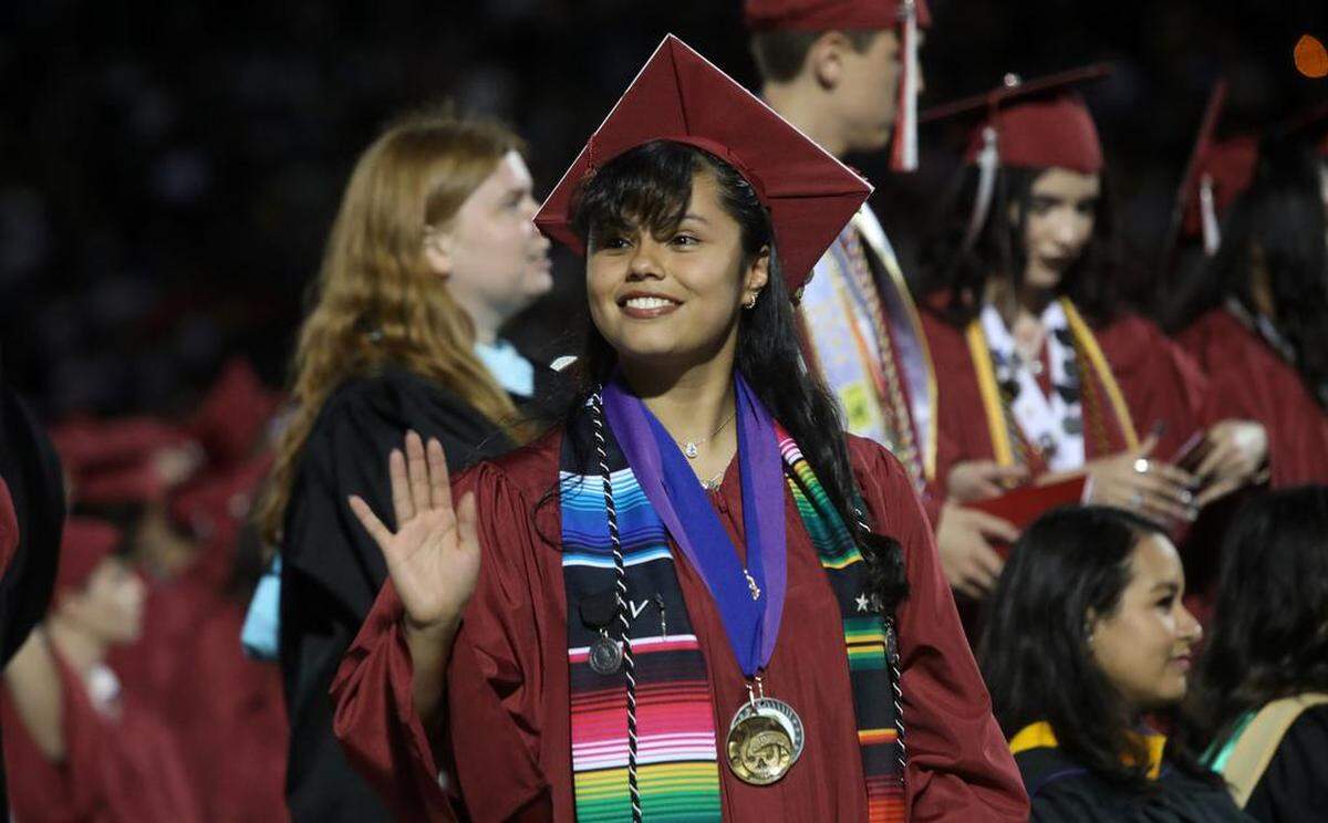 A graduate waves at someone in the crowd during the first graduation ceremony for Matilda Torres High School at Madera Memorial Stadium on June 10, 2023.