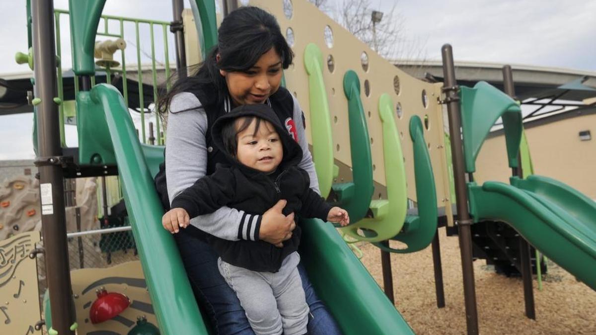 Maribel Lopez holds her child Savannah Cervantes as they slide at Romain Park’s new children’s playground in January 2016.