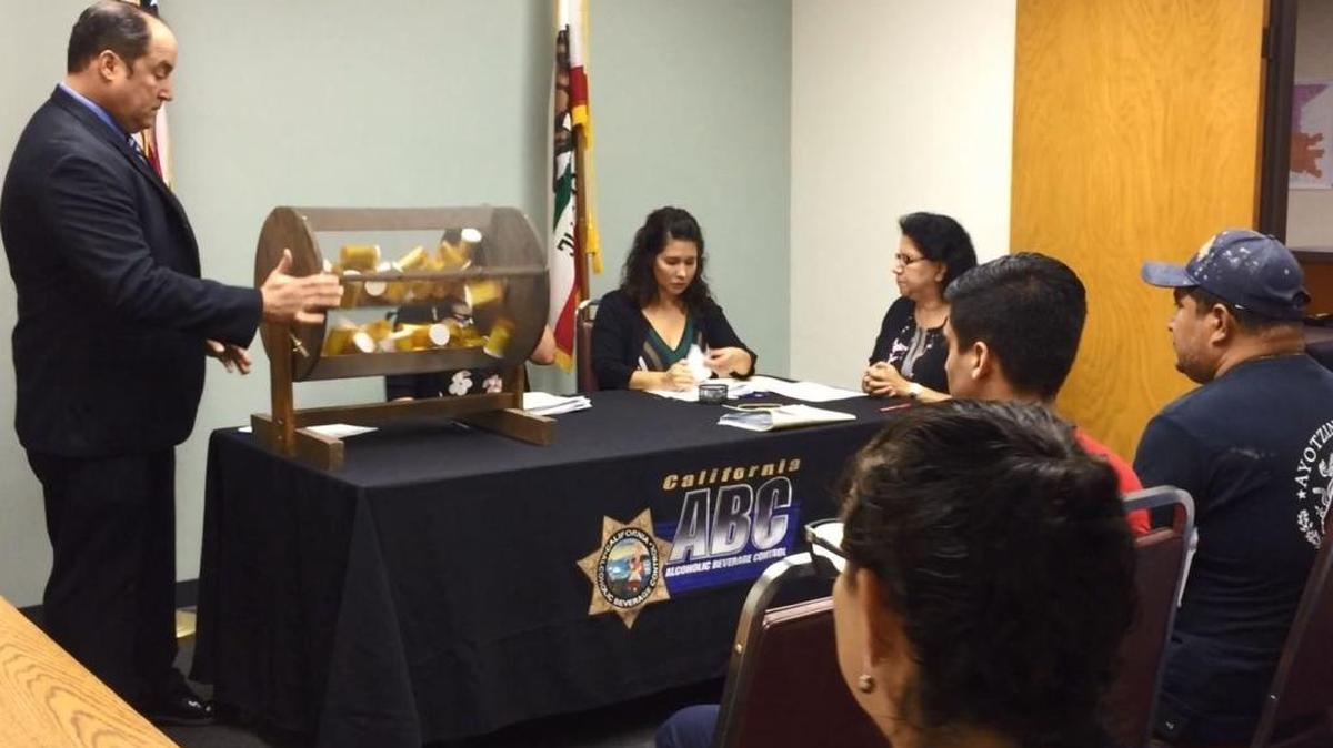 Jason Montgomery, supervising agent for the state Alcoholic Beverage Control, turns a cage containing bottles with names of liquor license applicants in a drawing Tuesday in Fresno as ABC staff and applicants watch.