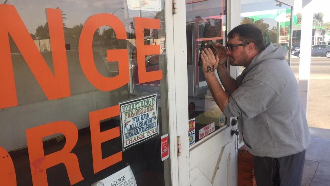 Customer Brandon Pasnick looks through the front door of The Orange Store in Fresno, which closed last month.