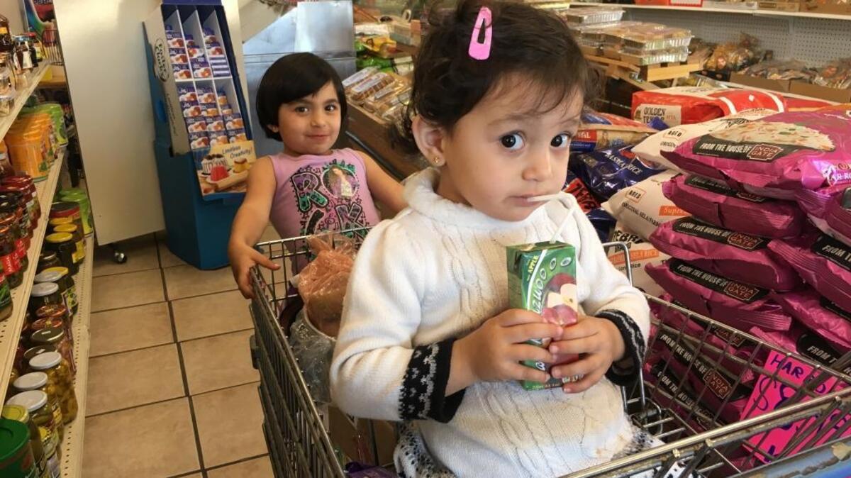 Sham Ismail Abdulkader, 2, drinks juice while waiting for her mother to finish grocery shopping at Dunia Market in central Fresno. Sham’s sister Shahed Ismail Abdulkader, 4, rides on the edge of the shopping cart. The trip to the market on Nov. 2 was the family’s first since arriving in Fresno as Syrian refugees.