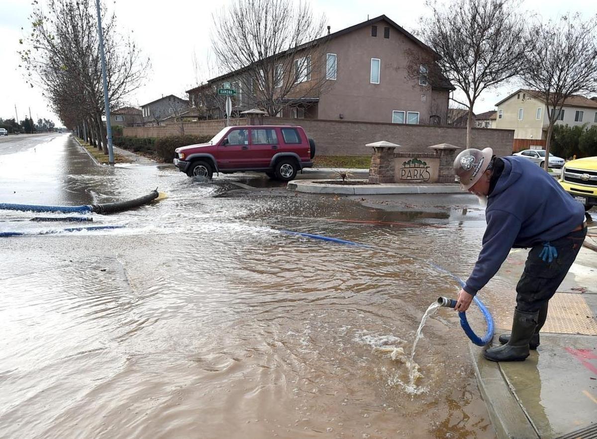 Kirk Wilson of Floyd Johnson Construction places a hose into a gutter to carry away pumped water from Gould Canal, which breeched its banks early Wednesday morning, Dec. 10, between Ashlan and Shields avenues.