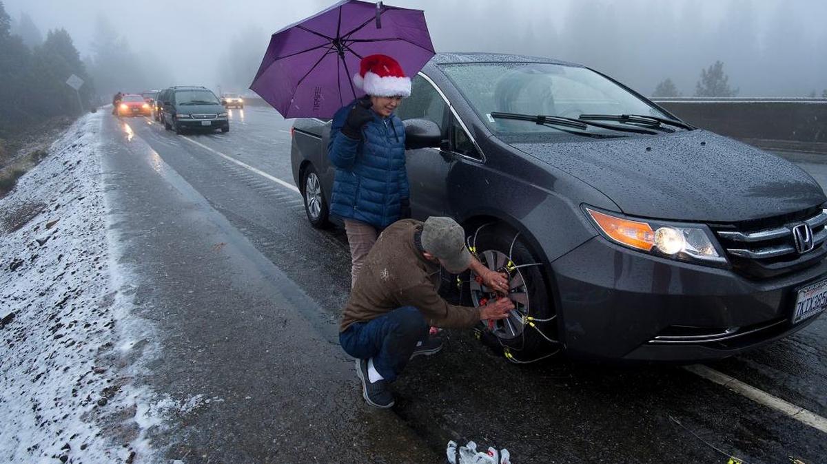 As the snow falls, Holly Ly, left, and Charles Luong of San Diego, struggle to put tire chains on their car in Camino on Thursday, Dec. 24, 2015. Snow levels dropped to about 2,000 feet elevation and motorists on US 50 were required to install chains just east of Placerville, Calif.