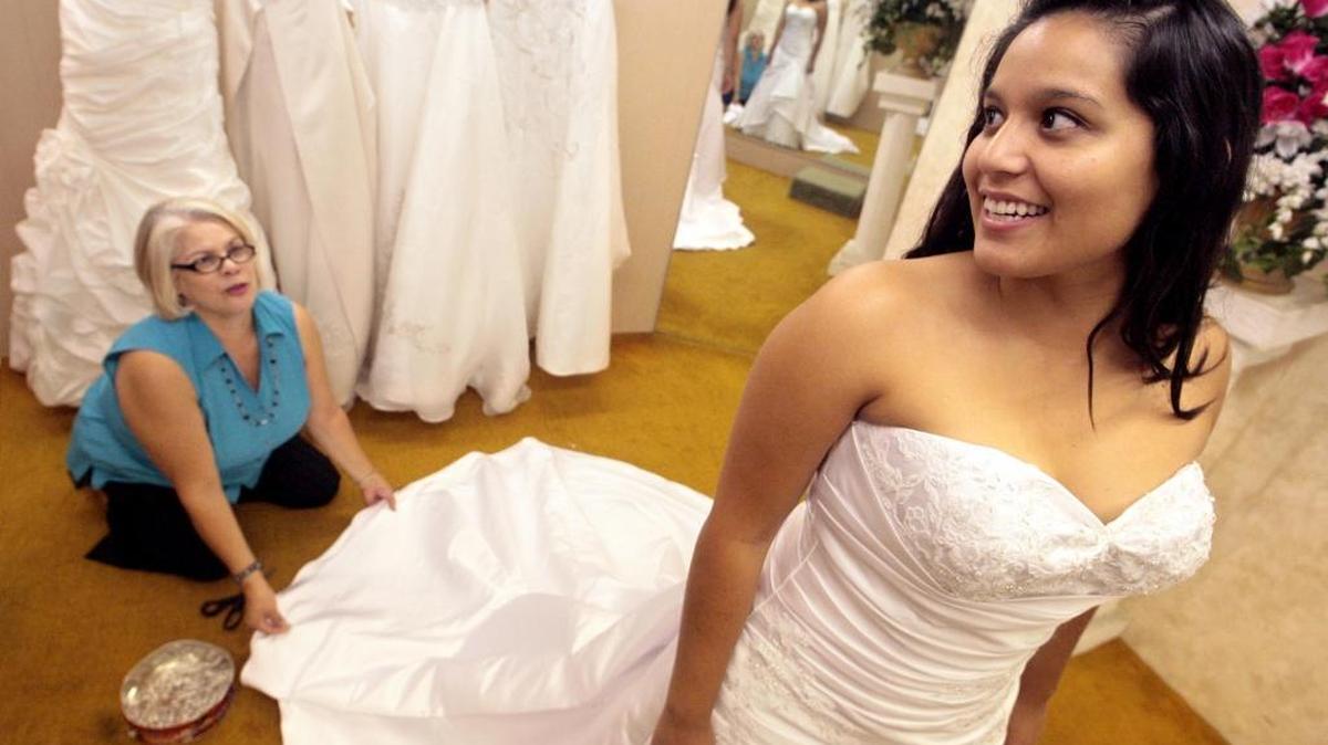 Victoria Hernandez looks in a mirror as she is fitted with a wedding gown at Luftenburg’s Bridal in a 2010 photo. Luftenburg bridal consultant Effie Rodriguez helps out. The shop, which has operated for 75 years, will be closed by its owners.
