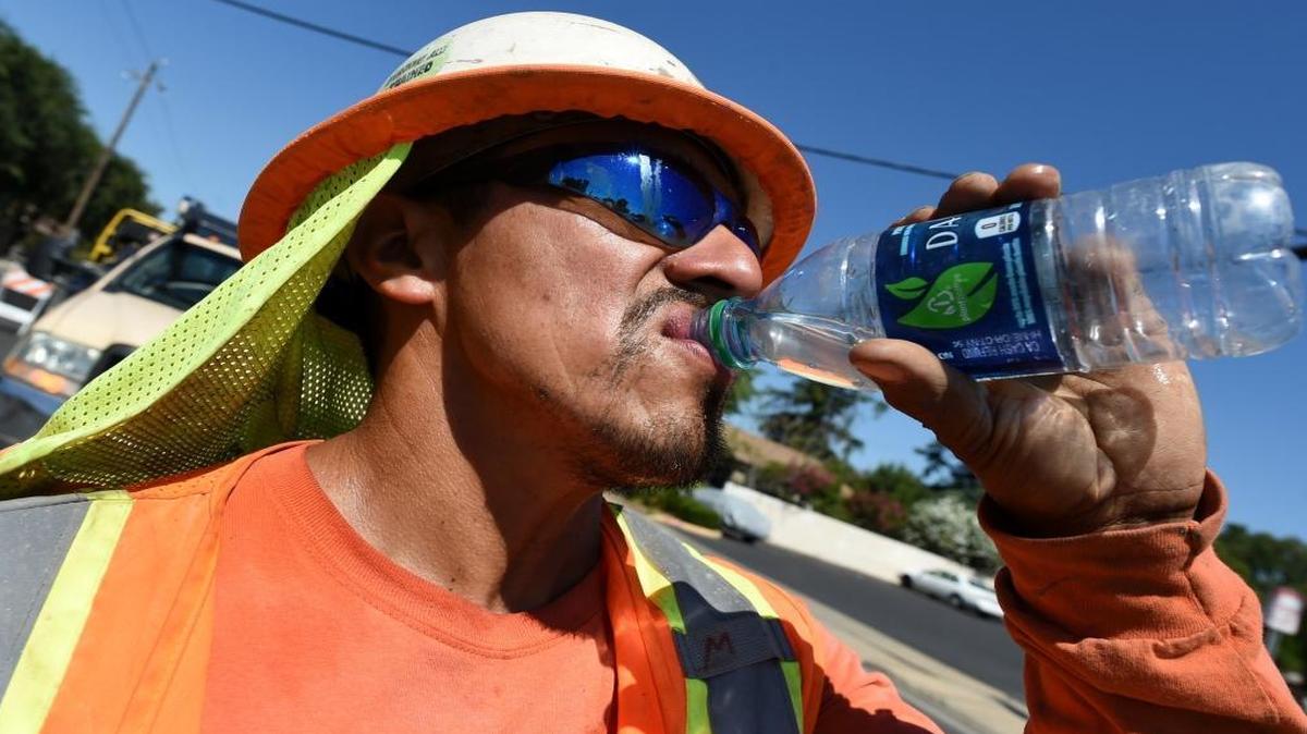 Miguel Lunar of Madco Electric takes a swig of cold water during work at Palm and Shields avenues to install traffic sensors under the roadway surface on June 21.