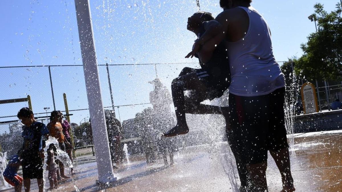 Bryndon Williams carries his stepdaughter Kedreyah Venson, 8, through the jets of water at Dickey Playground on a hot Thursday afternoon, June 22, 2017 in Fresno, Calif.