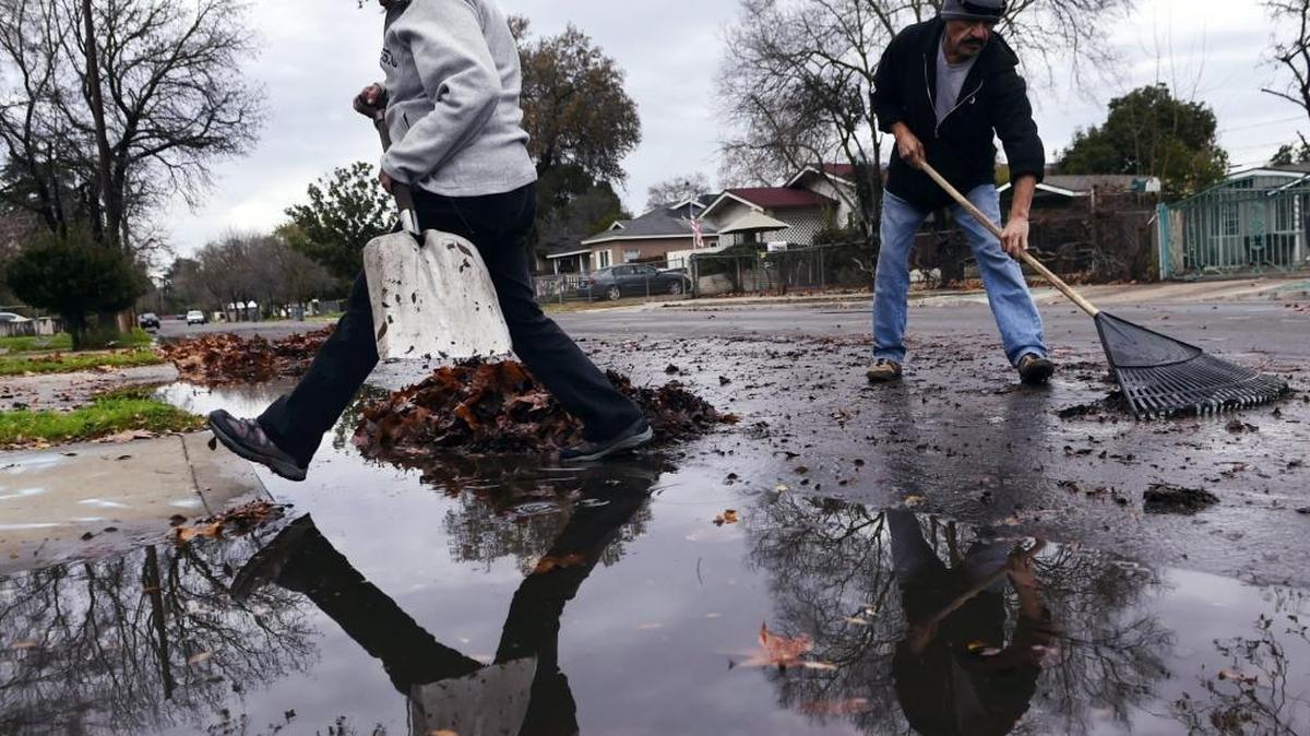 Dora Vela, left, steps across standing water as Tony Ramos continues raking the gutter clear of leaves to allow drainage following a storm Wednesday afternoon, Jan. 4, 2016, in Fresno, Calif. About 0.64 inches of rain was recorded in Fresno by noon Wednesday. A second storm is expected this weekend, according to the National Weather Service.