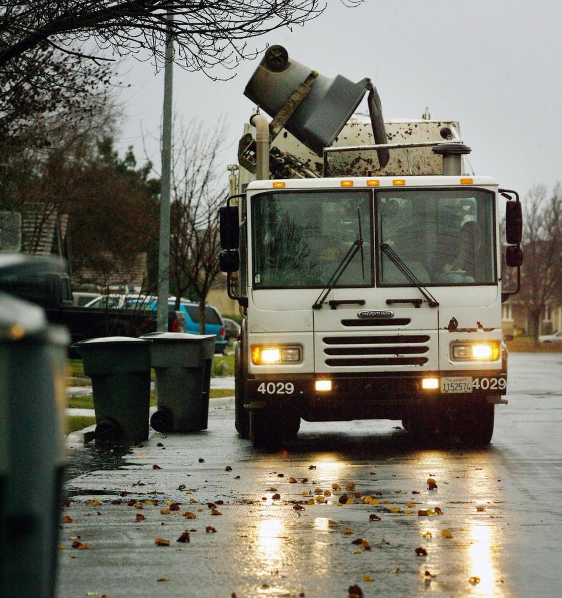 A truck empties a wheeled residential trash container into its hopper as it moves along a Fresno street in this Bee file photo.