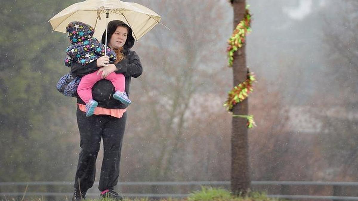 Alyssa Kemley of Auberry carries her 17-month-old daughter Annmarie as they pass a tinsel-wrapped tree on a rainy walk to visit some friends in town on Monday, Dec. 21, 2015, in Oakhurst.