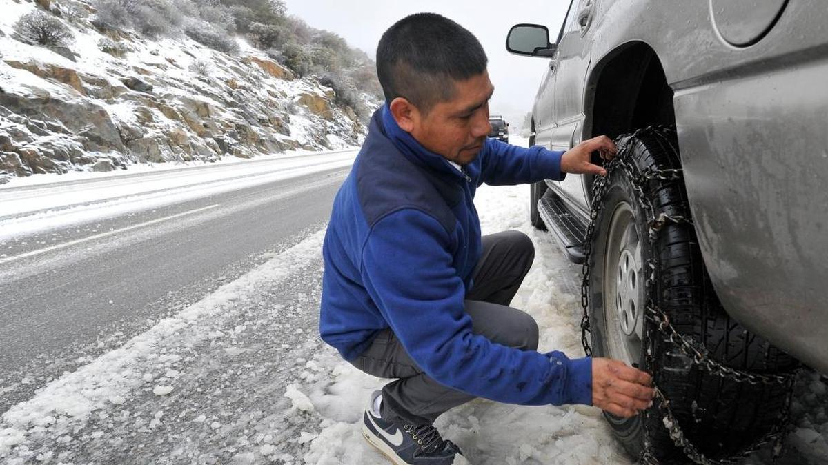 Ramiro Garcia of Fresno puts chains on his tires while heading up Highway 168 to Shaver Lake in this 2015 photo. CHP officer Robert Montano says drivers should get familiar with tire chains before heading to the Sierra.
