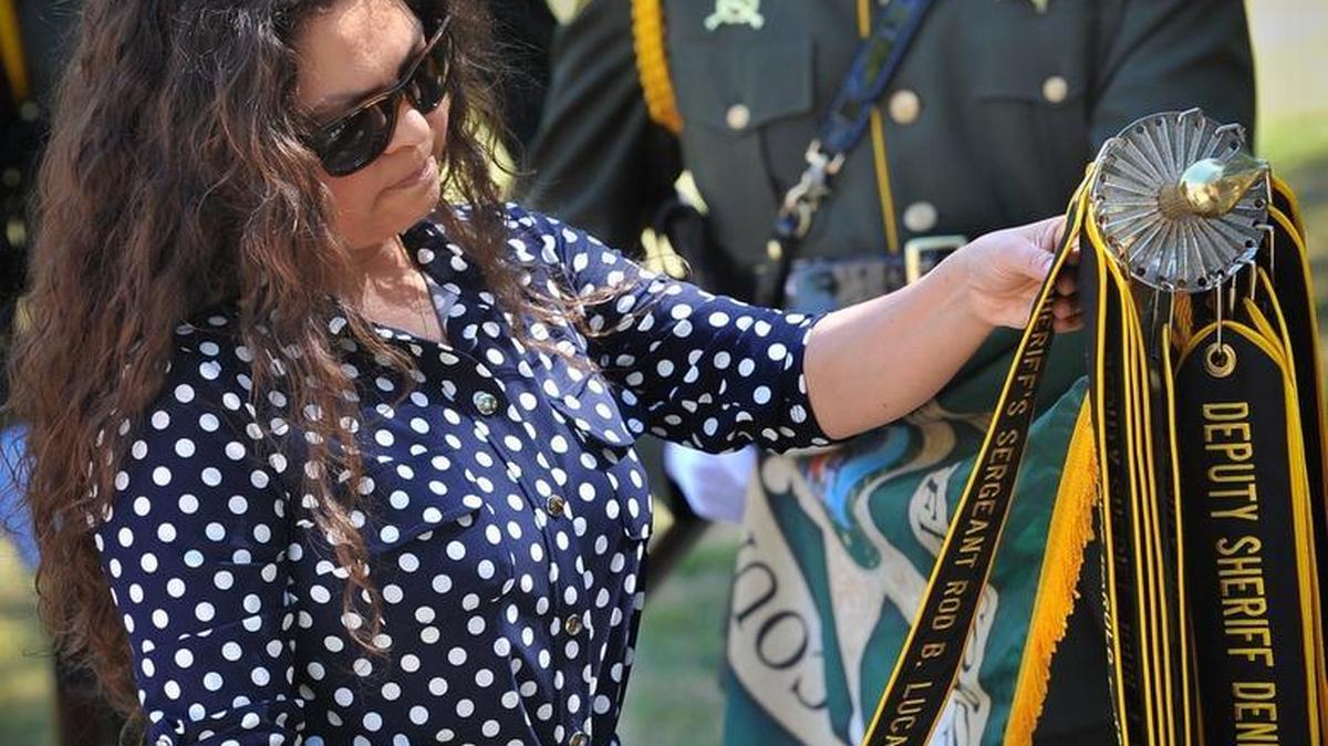 Jamie Lucas, wife of late Fresno County Sheriff’s Sergeant Rod Lucas, pauses to look at the streamer with her husband’s name after she added it to the flagstaff with the department flag and streamers with names of all those in the sheriff’s department killed in the line of duty since the county was formed in 1856, held by Fresno County Sheriffs Department Deputy Tyler Hitter, during the end of watch streamer ceremony on the steps of the sheriff’s office, Thursday morning. Lucas was killed in an accidental shooting Oct. 31, 2016.