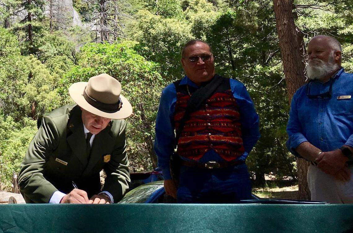 Yosemite National Park Superintendent Michael Reynolds, left, signs an agreement next to Bill Leonard, chairman of the American Indian Council of Mariposa County/Southern Sierra Miwuk Nation, at the Wahhoga village site in Yosemite Valley on June 1, 2018 as Scott Carpenter, Yosemite's program manager for cultural resources, far right, looks on.