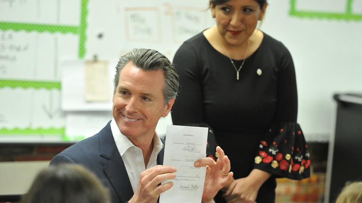 California Gov. Gavin Newsom holds up AB-72, the first bill he signed as governor, in front of a Riverview Elementary School classroom full of students as state Sen. Melissa Hurtado looks on Wednesday afternoon, Feb. 13, 2019, east of Parlier.