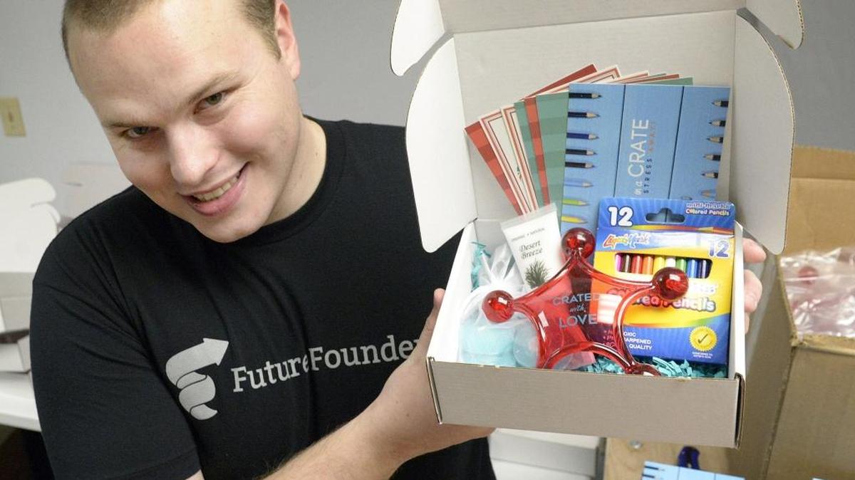 Tyler Turk, creator of Date in a Crate, holds up a box of February’s subscription box, including coloring books, crayons and stress massager.