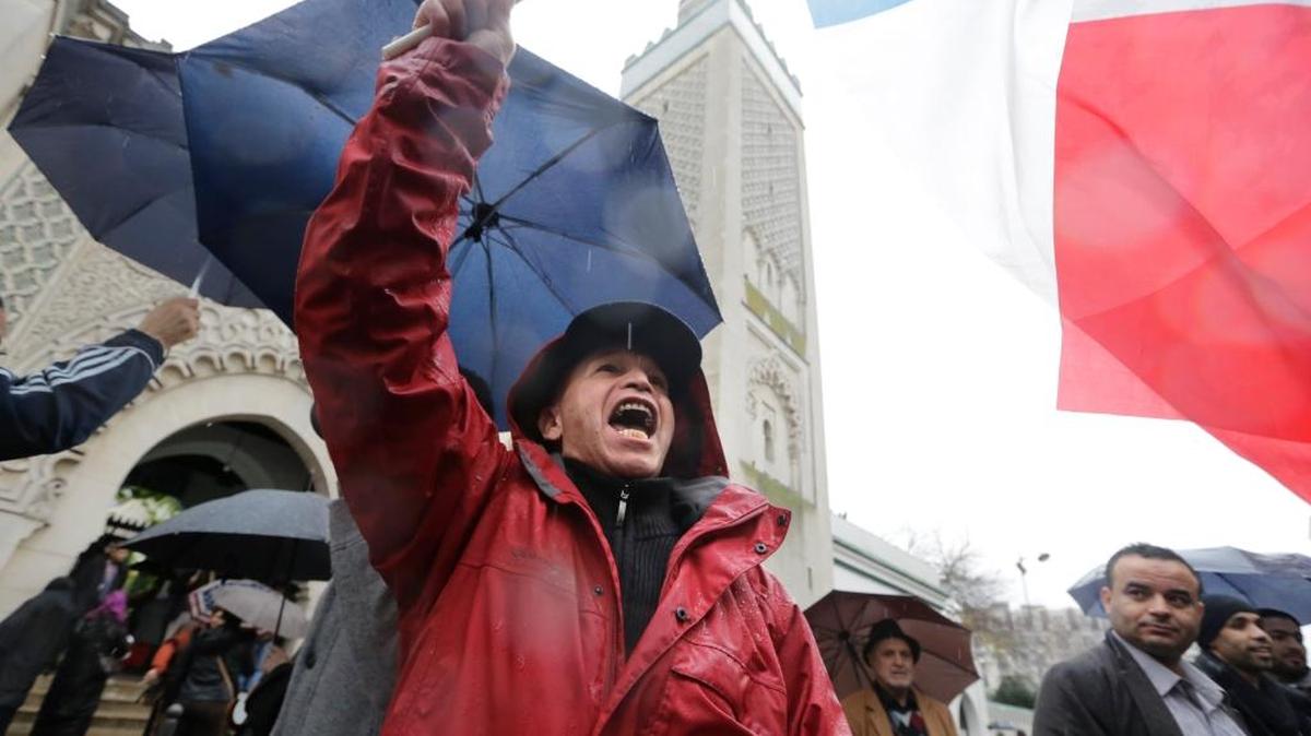A man identified only as Sherif waves the French flag and shouts anti-radical Islam slogans after Friday prayer at the Paris mosque Nov. 20. Cold rain extinguished the flickering candles and drenched the packets of flowers outside the Paris attacks sites, but people came anyway to pay tribute, to mourn, to reflect on their city’s losses one week later.