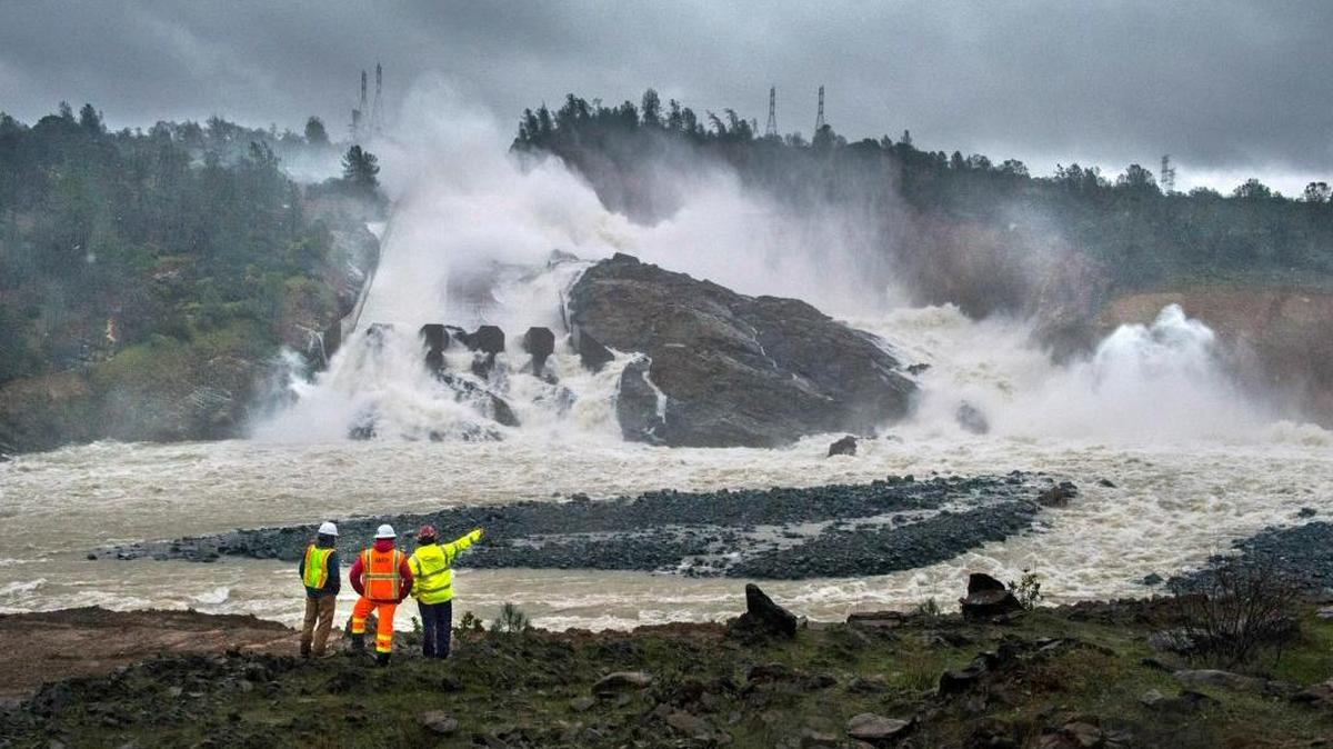 In this Feb. 20, 2017, photo, workers and a firefighter watch water pouring down Oroville Dam's damaged main spillway.