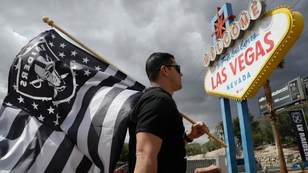 Matt Gutierrez carries an Oakland Raiders flag near a sign welcoming visitors to Las Vegas on Monday. NFL team owners approved the move of the Raiders to Las Vegas in a vote at an NFL football annual meeting in Phoenix.