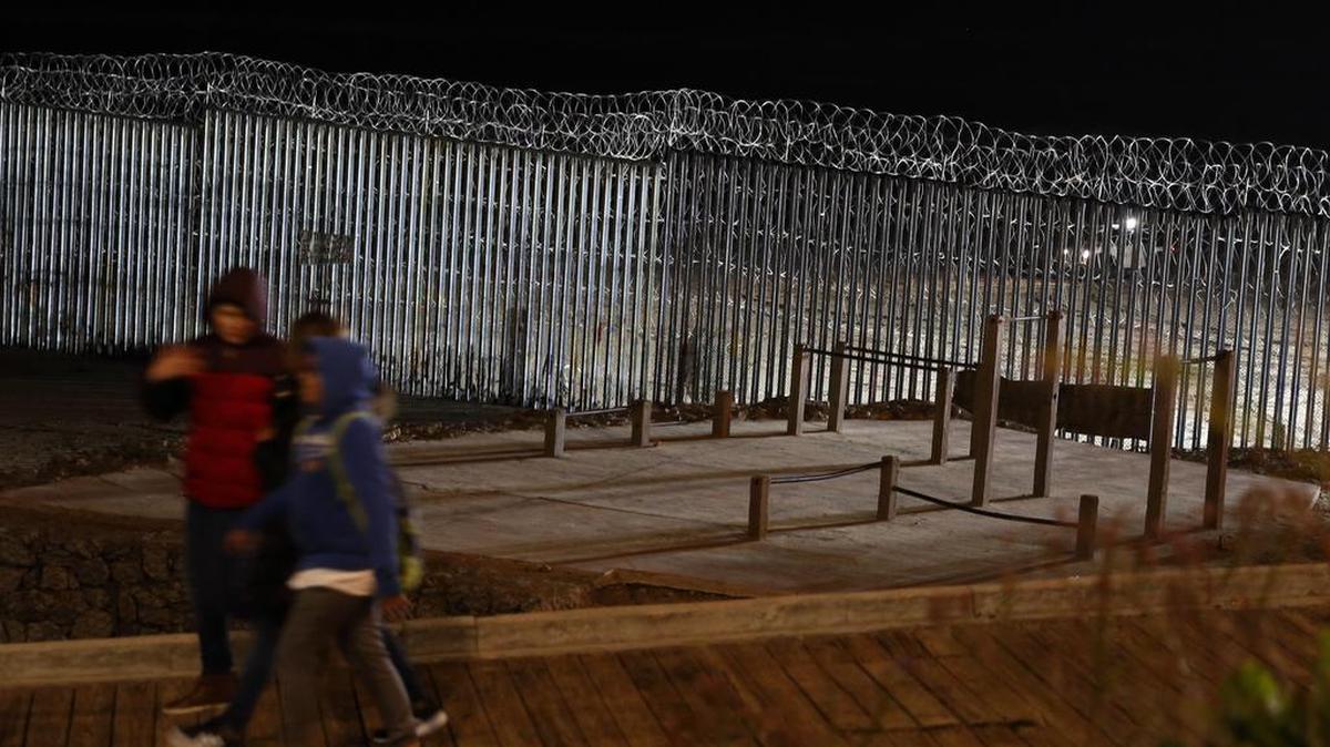 Floodlights from the U.S. illuminate the border wall, topped with razor wire, as people pass Monday at the beach in Tijuana, Mexico. With no breakthrough in sight, President Donald Trump was to argue his case to the nation Tuesday night that a “crisis” at the U.S.-Mexico border requires the long and invulnerable wall he's demanding before ending the partial government shutdown.