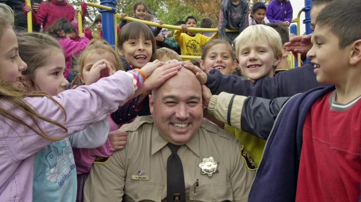 Stanislaus County sheriffs deputy Dennis Wallace, the DARE officer for Hart-Ransom School, shows off the results of his successful challenge to the students in 2004. With the program facing a funding crisis, Wallace bet the students that if they could raise at least $30,000 selling cookie dough he would shave his head. The kids came up with $32,000 and Wallace kept his promise. Wallace was killed while on duty near Hughson on Sunday.