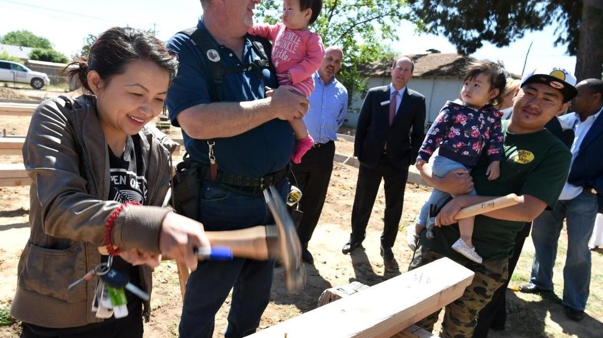 Habitat for Humanity construction manager Rick O'Daniel tends to 1-year-old Bethany Vang, as her mom, Yang Vue ceremoniously hammers a nail into a wall section. Her brother, Meng Vue, right, holds her other daughter, Allison Vang, 2. Yang Vue and family were one of two families who learned Monday that they were chosen by Habitat for Humanity to have a home built.
