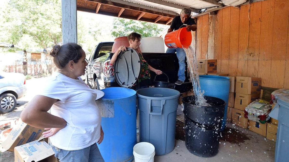 
Juana Garcia, 49, watches as volunteers Donna Johnson, 72, center, and Ruben Perez, 68, deliver non-potable water to barrels on her back porch in East Porterville June 4. Garcia, who suffers from lupus and arthritis, has difficulty lifting heavy objects and making the 15-minute walk with her children to a local church for showers several times a week. Residents say their existing health issues have been exacerbated by the dusty air and dry taps.
