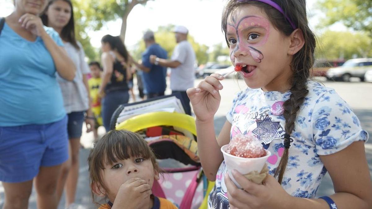 Nevaeh Warner, right, 7, finishes up a sucker before moving to a snow cone at National Night Out, hosted by the Fresno Police Department.