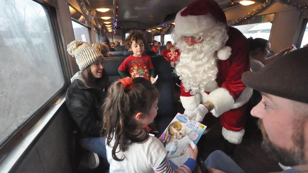Santa Claus gives a book to Aydia Raiff, 5, of Pittsfield, Mass., as Cruz Bermudez, 3, of Lenox, Mass., waits his turn, during their ride Sunday, Dec. 20, 2015.