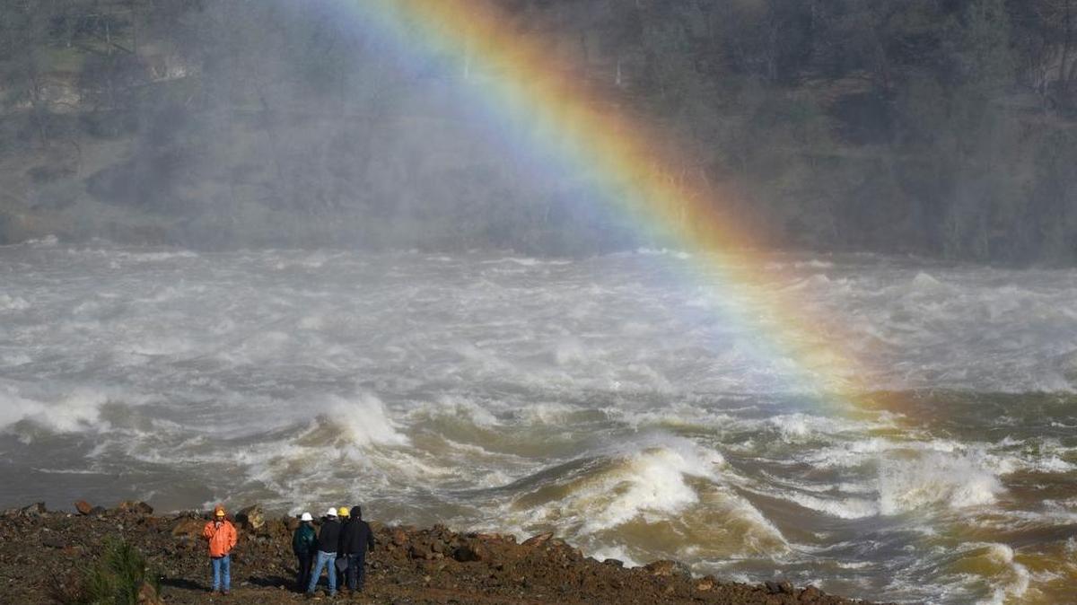 A rainbow is seen next to Department of Water Resources workers on the banks of the Feather River as water is released down the damaged primary spillway at 100,000 cubic feet per second in Oroville on Feb. 14, 2017.