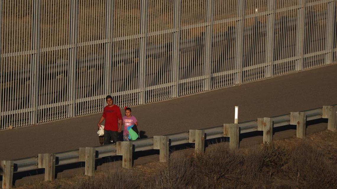 A migrant man walks with a girl along a secondary border fence in San Ysidro, Calif. toward border patrol agents waiting further down the road to detain them, after they crossed under the U.S. border fence from in Playas de Tijuana, Mexico, Tuesday, Dec. 4, 2018. Discouraged by the long wait to apply for asylum through official ports of entry, many Central American migrants from recent caravans are choosing to cross the U.S. border wall and hand themselves in to border patrol agents. (AP Photo/Rebecca Blackwell)