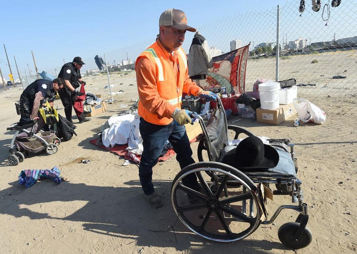 Ray Velasquez, of the city’s Sanitation Department, removes a wheelchair from an unattended homeless camp as Fresno police officers sort through items during a clean up along G Street, Wednesday morning, Aug. 14, 2018.