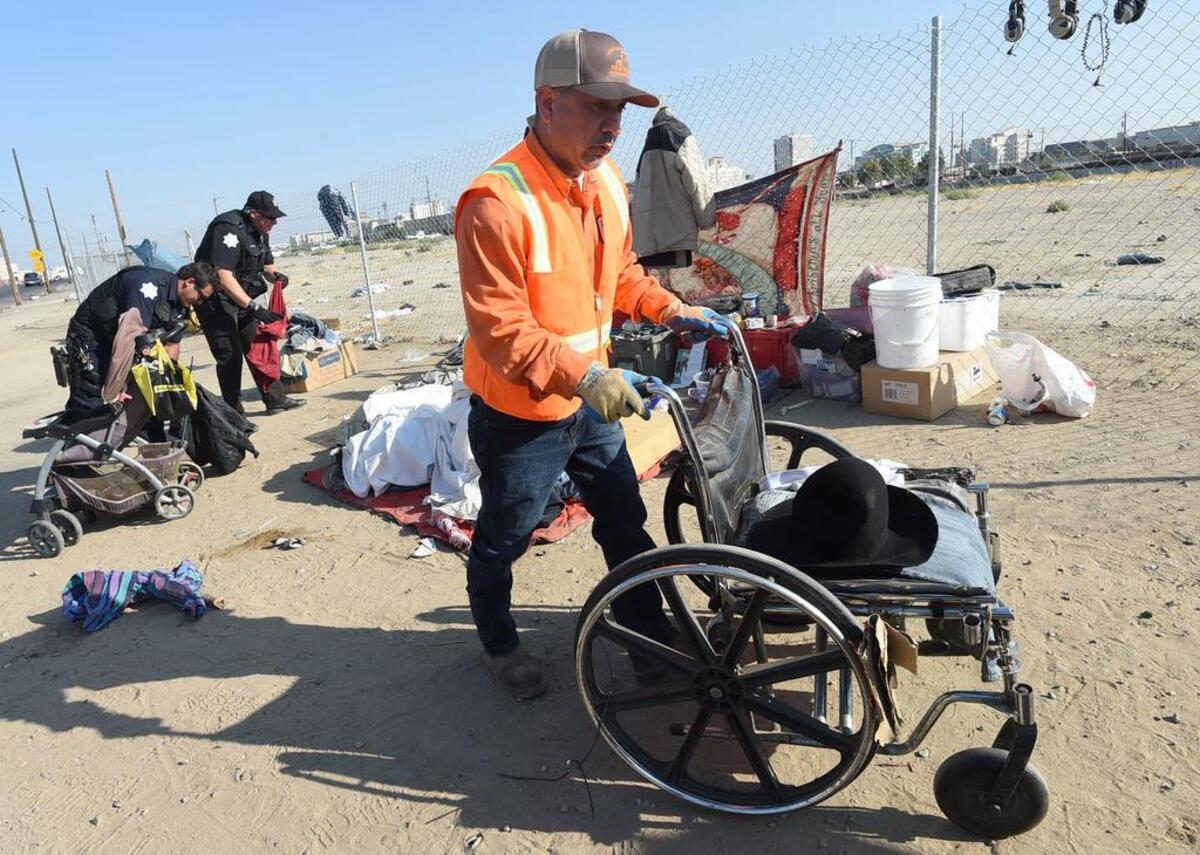 Ray Velasquez, of the city’s Sanitation Department, removes a wheelchair from an unattended homeless camp as Fresno police officers sort through items during a clean up along G Street, Wednesday morning, Aug. 14, 2018.