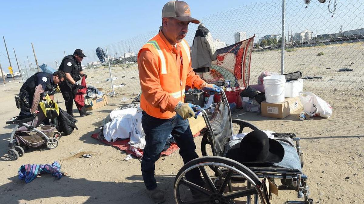 Ray Velasquez, of the city’s Sanitation Department, removes a wheelchair from an unattended homeless camp as Fresno police officers sort through items during a clean up along G Street, Wednesday morning, Aug. 14, 2018.