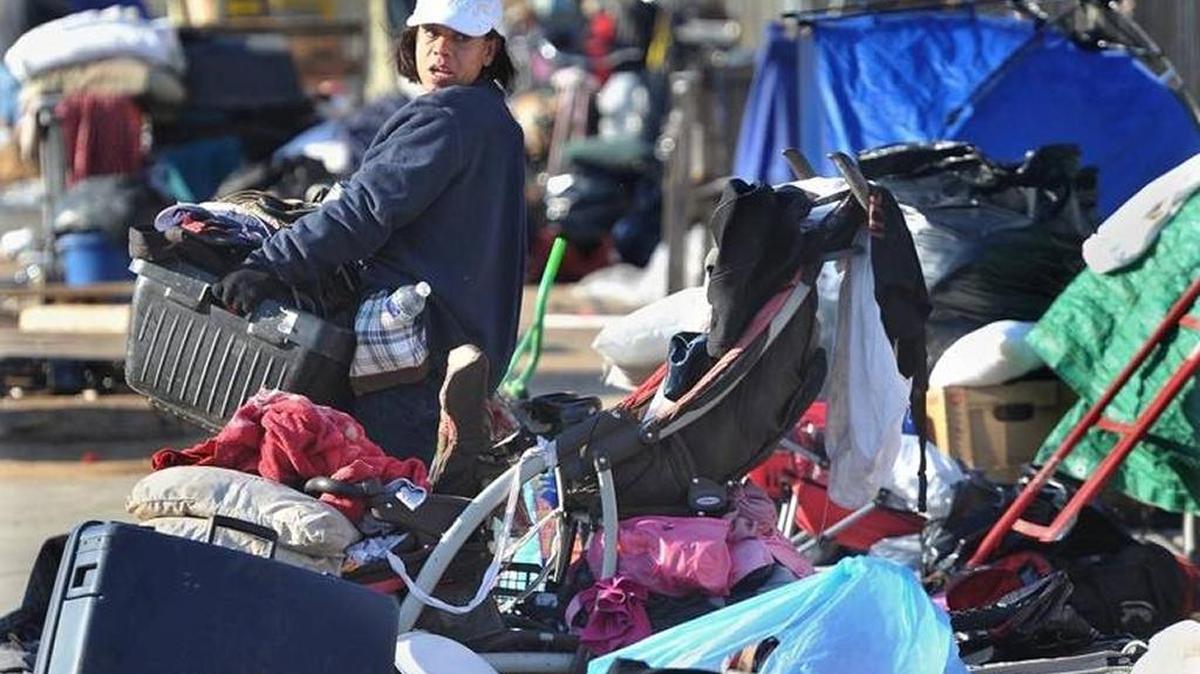 A woman packs up what she can carry as city crews move in Wednesday morning to clear the streets of refuse at a camp near the Poverello House.