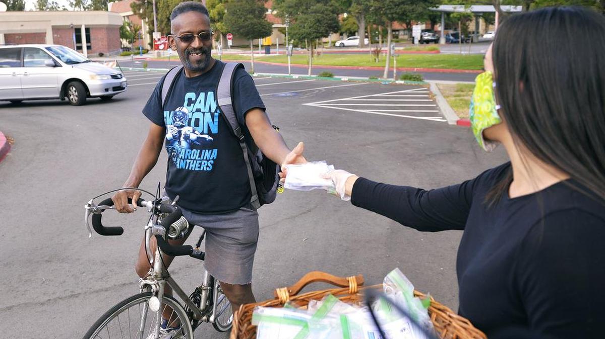 Annalisa Perea, right, hands a free face mask to Seth Wright, left, who went through the line on his bicycle at a free face mask distribution event in the south parking lot at Fresno City College on May 18 in Fresno. Organized by Fresno City Councilmember Esmeralda Soria and Perea, a State Center Community College District trustee, about 4,000 masks were collected for the distribution.
