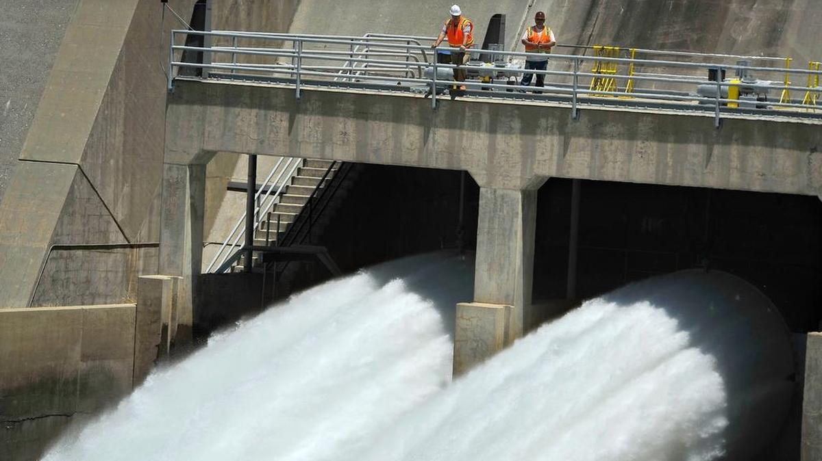Dwarfed by the thunderous roar of releases of Millerton Lake water from a pair of huge Friant Dam valves, totaling 1,000 cubic feet per second, Michael Wolfe, left, Friant Dam supervisor of hydrologic technicians, and Darrin Williams, Friant Dam maintenence supervisor, observe the historic release in July 2015.