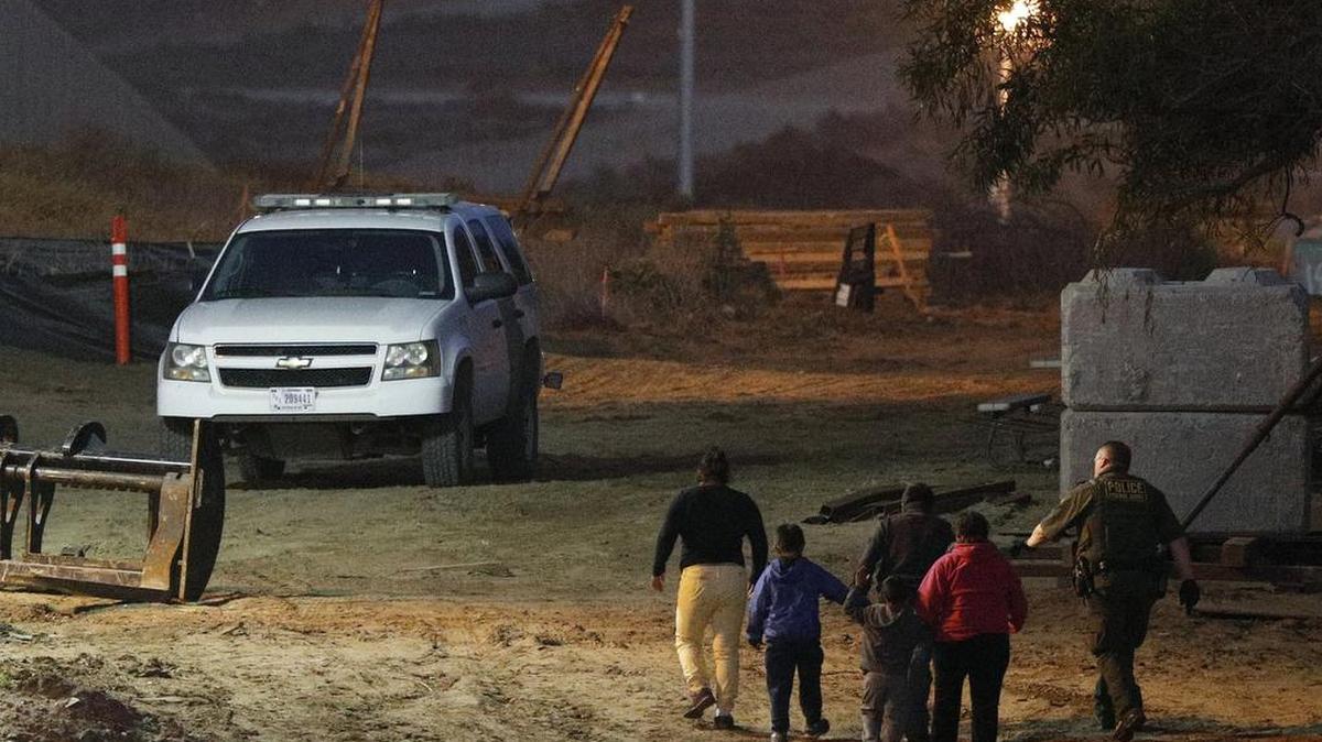 Migrants are escorted by a U.S. Border Patrol agent as they are detained after climbing over the border wall from Playas de Tijuana, Mexico, to San Ysidro last December. The Trump administration’s effort to make asylum seekers wait in Mexico explicitly targets Spanish-speakers and people from Latin America, according to internal guidelines of a highly touted strategy to address the burgeoning number of Central Americans arriving at U.S. borders.