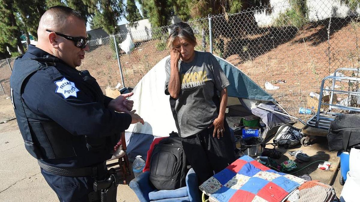 Elena Zurala listens as Fresno police officer Albert Avelar advises her on what she can take with her during a clean up of an alley in central Fresno, along Highway 41, Wednesday, Aug. 14, 2018. She was offered assistance and declined it.