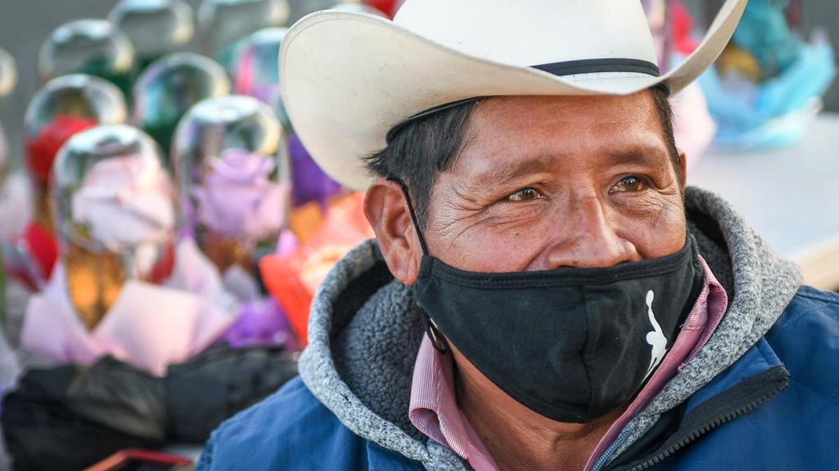 Guillermo Lozano smiles behind his COVID-19 mask while sitting in a chair on side of the road in rural Madera County where he sells flowers and gifts in this December photo.