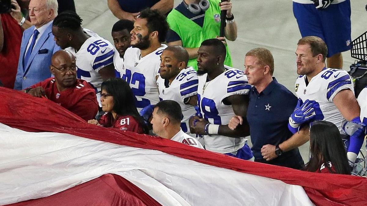 Dallas Cowboys owner Jerry Jones, left, and head coach Jason Garrett, second from right, stand with their players for the national anthem prior to an NFL football game against the Arizona Cardinals in Glendale, Ariz.