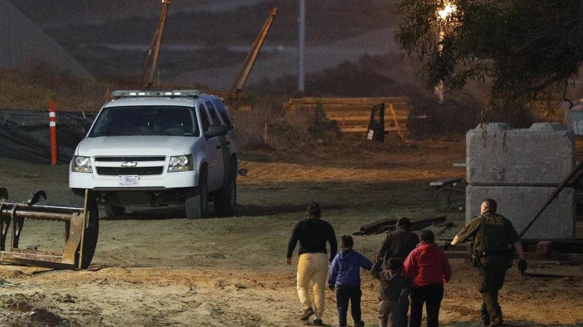 In this Dec. 3, 2018 photo, migrants are escorted by a U.S. Border Patrol agent as they are detained after climbing over the border wall from Playas de Tijuana, Mexico, to San Ysidro, Calif. The Trump administration expects to launch a policy that forces people seeking asylum to wait in Mexico while their cases wind through U.S. courts, an official said, marking one of the most significant changes to the immigration system of Donald Trump's presidency.