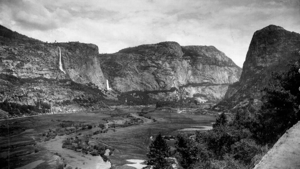 A photo taken of Hetch Hetchy Valley before it was flooded reveals a broad valley of the Tuolumne River. The river meandered westward, fed by the twin Wapama Falls.