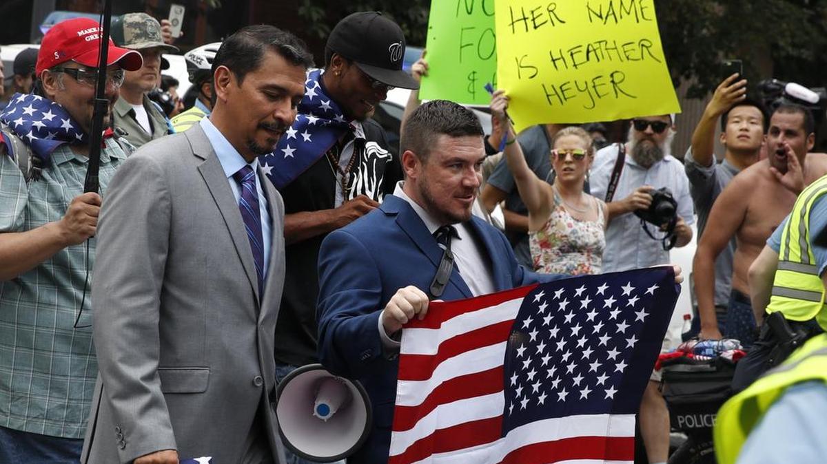 White nationalist Jason Kessler, center, walks to the White House to rally on the one-year anniversary of the Charlottesville “Unite the Right” rally, Sunday, Aug. 12, 2018, in Washington, D.C. In the background is a protester holding a sign referencing the woman who died in last year’s rally that says, “her name is Heather Heyer.”