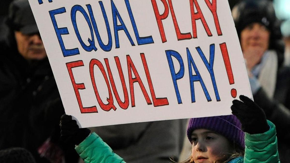 A girl holds up a sign for equal pay for the U.S. women soccer players in 2019. March 15 marks “Equal Pay Day,” the date on the calendar each year through which a woman must work to get paid the same amount a man did the previous year.