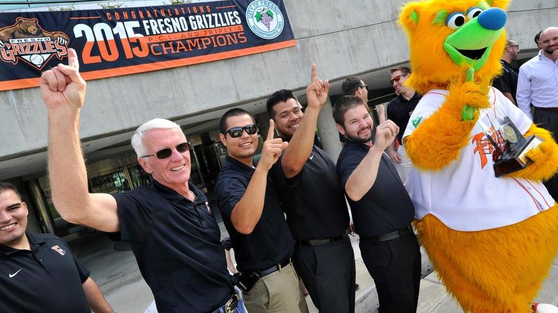 Fresno Grizzlies managing general partner Chris Cummings, left, raises his arm in celebration during a City Hall ceremony with team staff and mascot Parker honoring the team’s Pacific Coast League and Triple-A championships. Cummings and his partners at Fresno Baseball Club have been trying to sell the team for almost two years.
