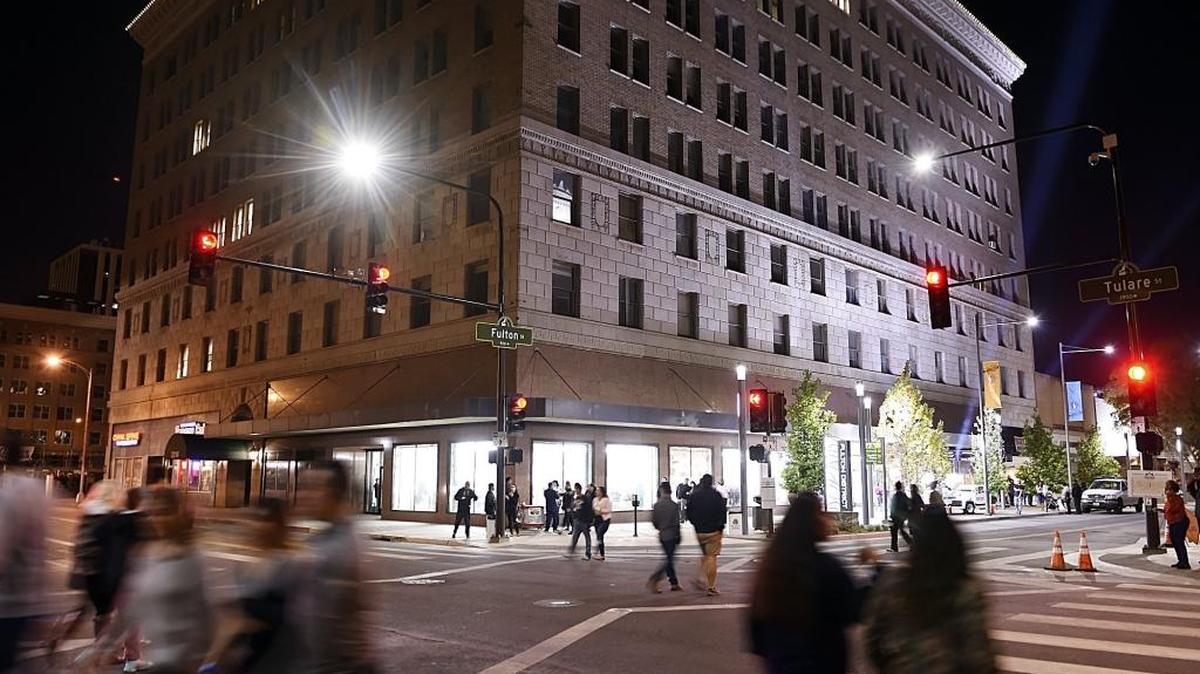 Peatones cruzan Tulare Street frente al iluminado T.W. Patterson Building en el centro de Fresno, tras la gran reapertura de Fulton Street, el 21 de octubre de 2017.