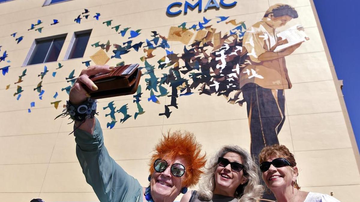 Jackie Ryle, izquierda, Rebecca Caraveo, centro, y Sally Caglia, derecha, posan para una foto antes del inicio de la ceremonia de inauguración y dedicación de un nuevo mural, al fondo, que rinde homenaje a los poetas y escritores del valle, el jueves 11 de mayo de 2017 por la mañana, en el centro de Fresno, California. El mural, en la cara sur del antiguo edificio del Fresno Bee y ahora CMAC, es un proyecto de Arte Americas con financiamirnto de McClatchy Fresno Art Endowment y el Fresno Arts Council. Contó con la presencia de los muralistas Francisco Letelier y Mauro Carrera. ERIC PAUL ZAMORA/THE FRESNO BEE