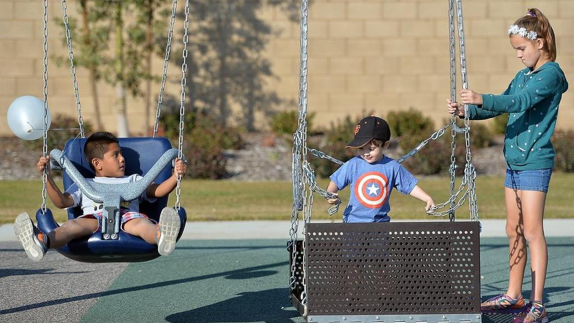From left, Eliseo Gonzalez, 6, Thomas Melton, 2, and Cayleigh Melton, 11, all of Fresno, ride on the swings as they celebrate the universally-accessible Inspiration Park in west Fresno. The swing on the right accommodates a wheelchair.