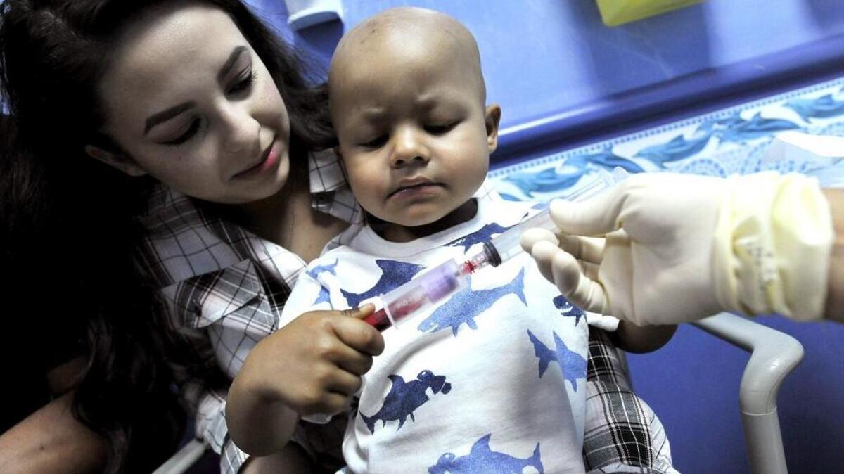 Oncology patient Noah Escobar, 2, helps by holding a vial which is filled with his blood, as he’s held by his mother Alexandria Escobar while being prepped for his last chemotherapy session at Valley Children’s Hospital.
