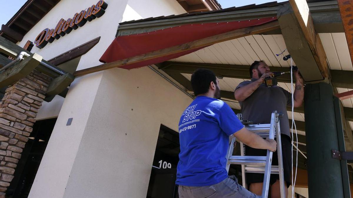 Workers install an outdoor speaker system at the Deli Delicious in Fig Garden Village in 2017.